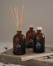 Three amber glass bottles with reed diffusers on a wooden surface.