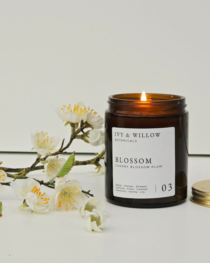 Candle with 'Ivy & Willow Botanicals' label next to white flowers on a light background