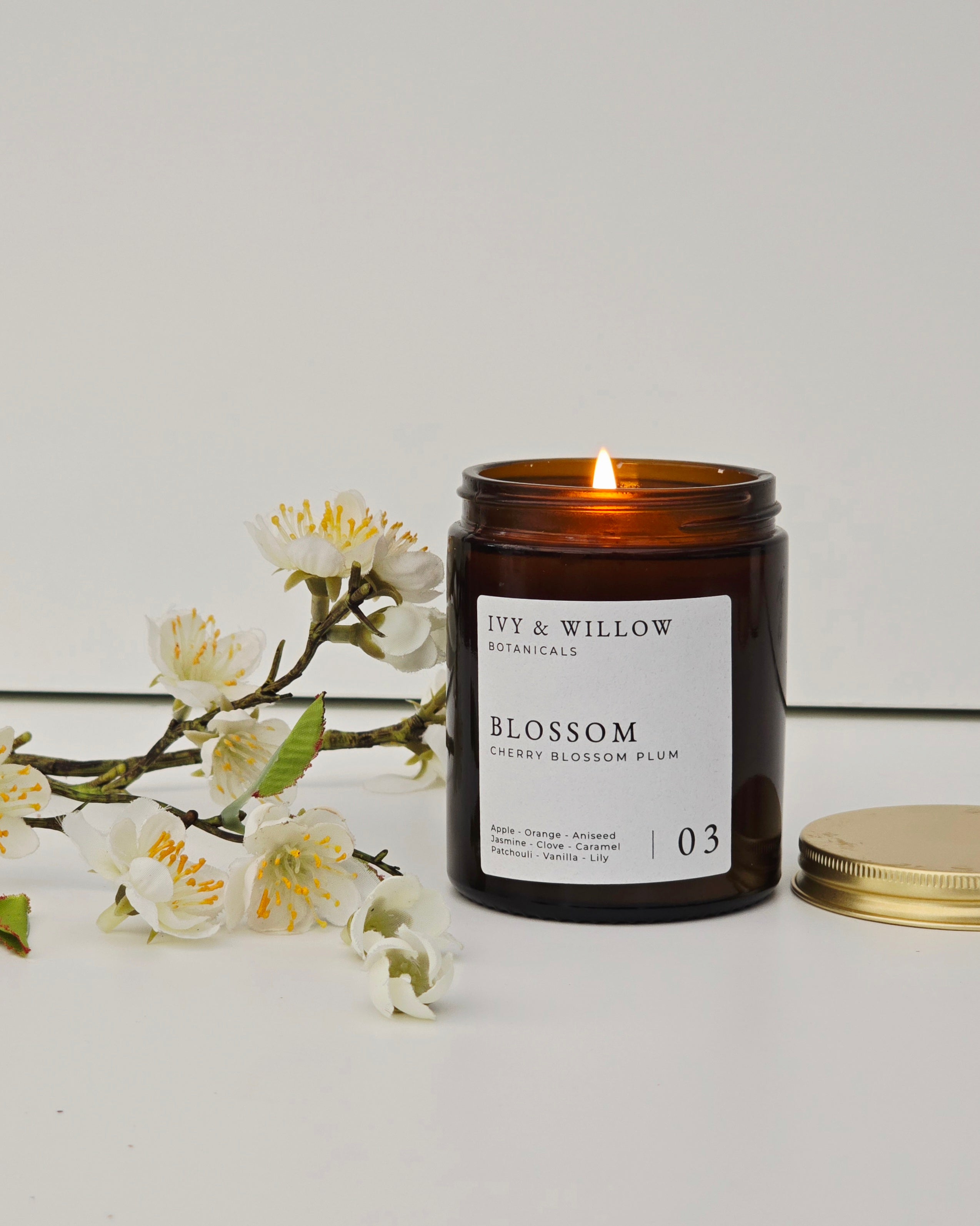 Candle with 'Ivy & Willow' label and floral arrangement on a light background