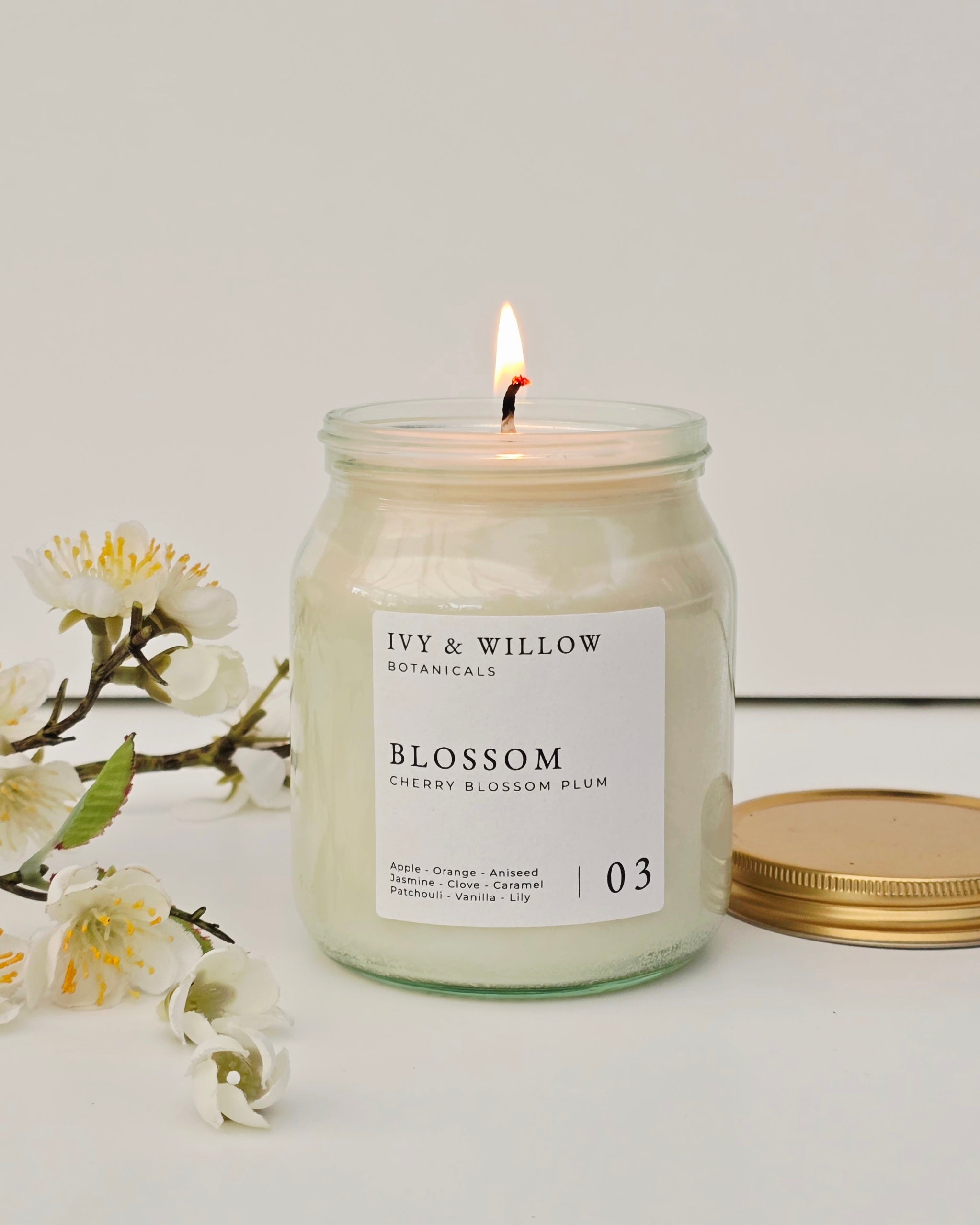 Candle in a jar labeled 'Ivy & Willow Botanicals' with flowers on a light background