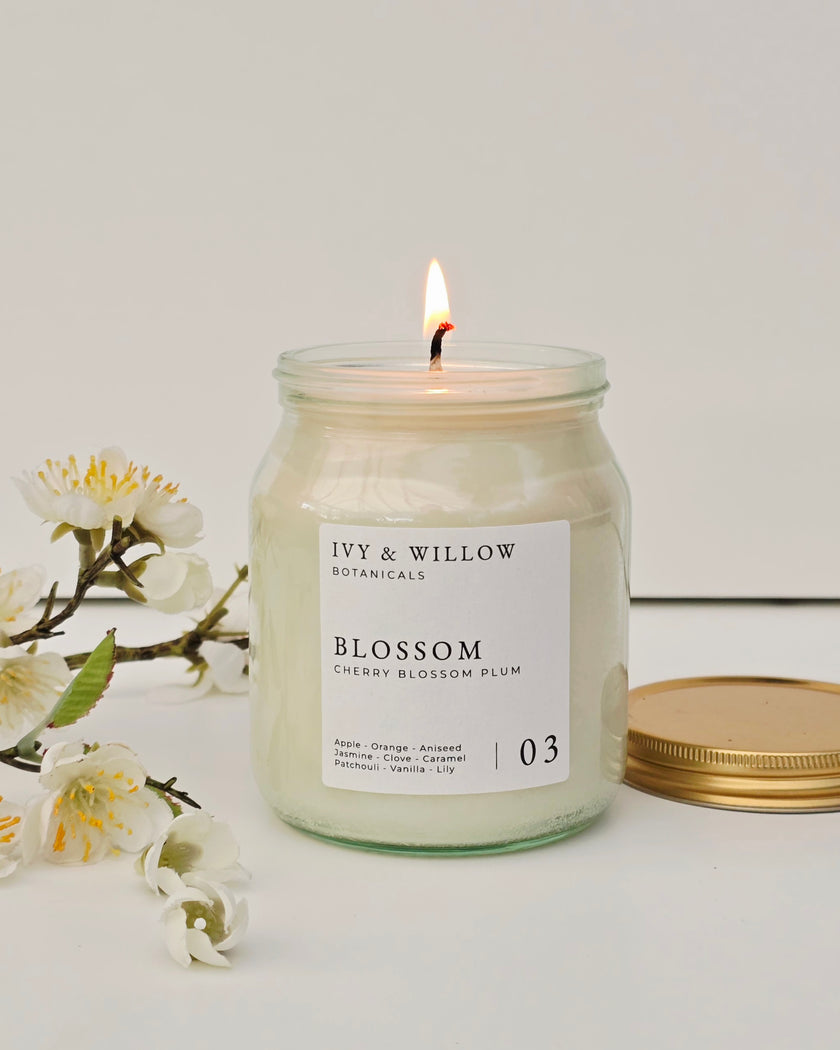 Candle in a jar labeled 'Ivy & Willow Botanicals' with flowers on a light background