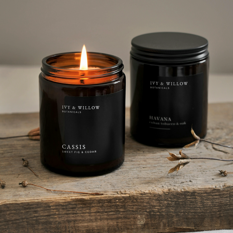 Two black candles from Ivy & Willow Botanicals on a wooden surface.