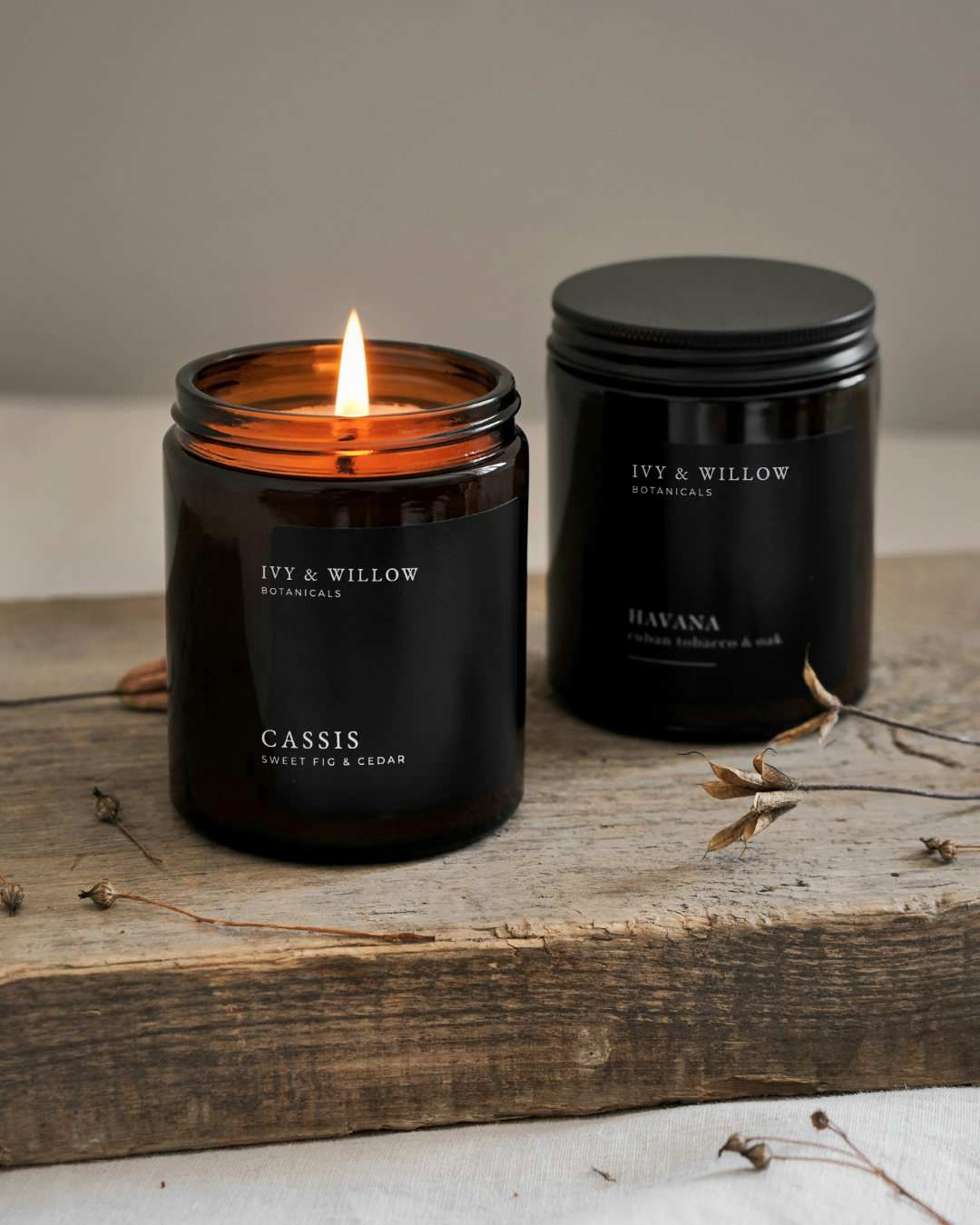 Two black candles from Ivy & Willow Botanicals on a wooden surface.