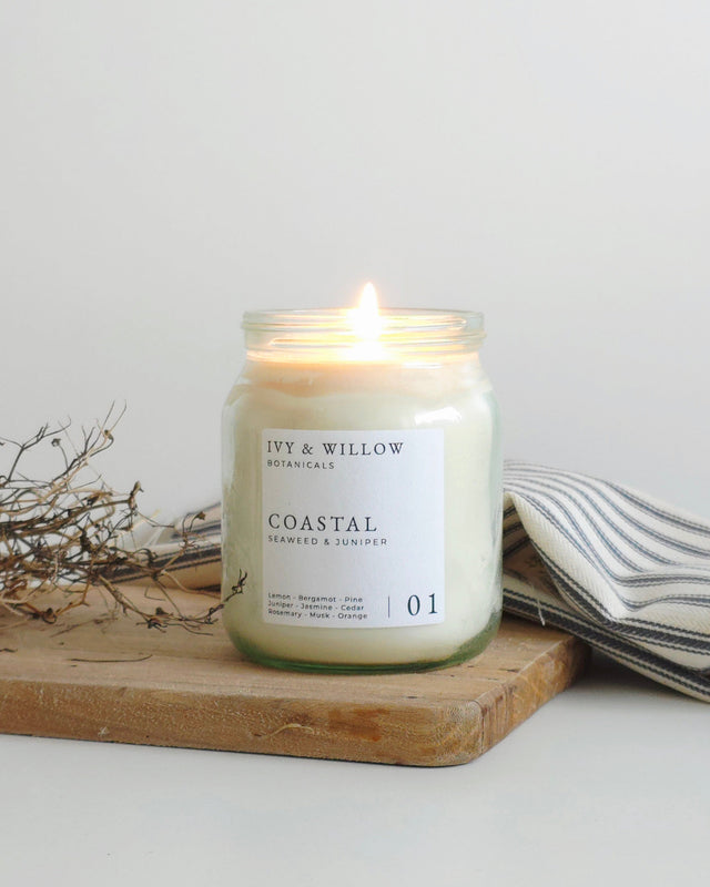 Candle in a glass jar labeled 'Coastal' by Ivy & Willow on a wooden board with a white background.