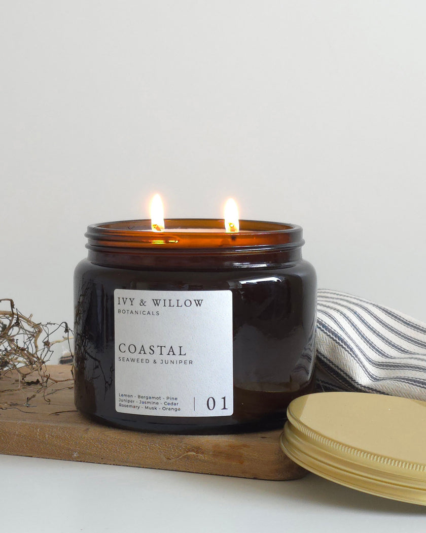 Black candle with a label on a wooden board, surrounded by dried plants and a striped cloth.