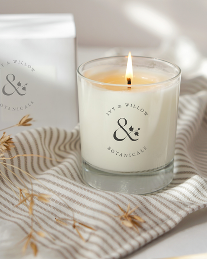 Lit candle with 'Ivy & Willow Botanicals' branding on a striped fabric background