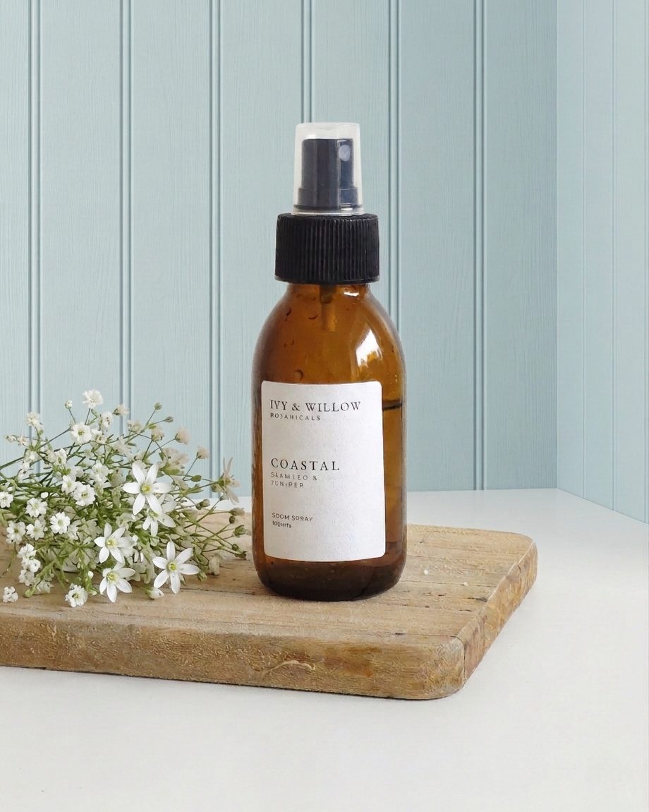 Brown spray bottle labeled 'Coastal' on a wooden board with white flowers against a light blue wall.