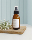 Brown spray bottle labeled 'Coastal' on a wooden board with white flowers against a light blue wall.