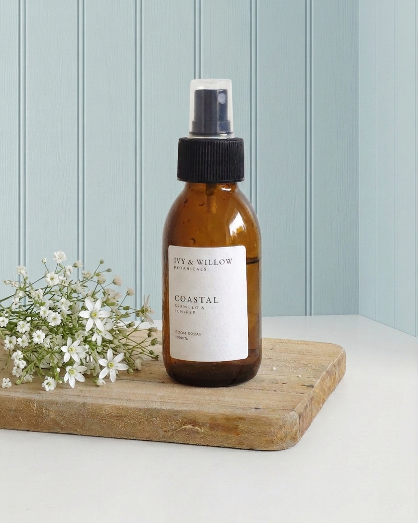 Brown spray bottle labeled 'Coastal' on a wooden board with white flowers against a light blue wall.