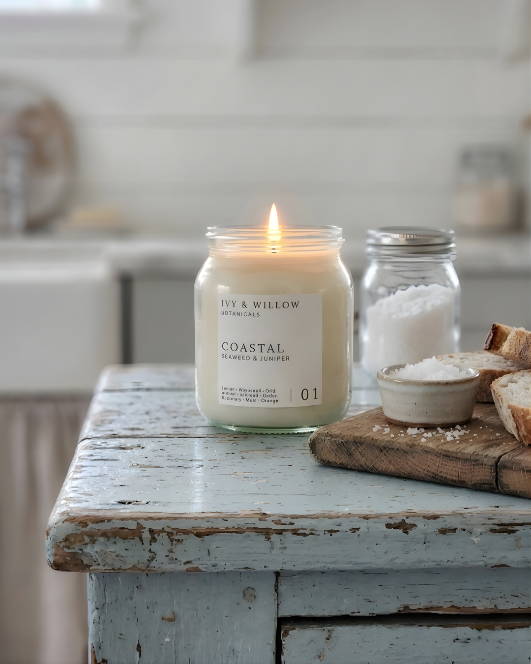 Jar candle labeled 'Coastal' on a rustic wooden table with a blurred kitchen background