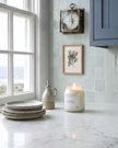Candle on a marble countertop with decorative plates, a bottle, and a framed picture in a kitchen setting.