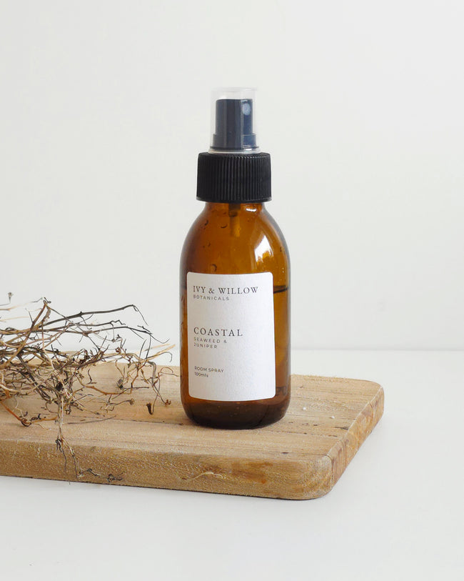 Brown spray bottle labeled 'Coastal' on a wooden board with dried plants on a white background