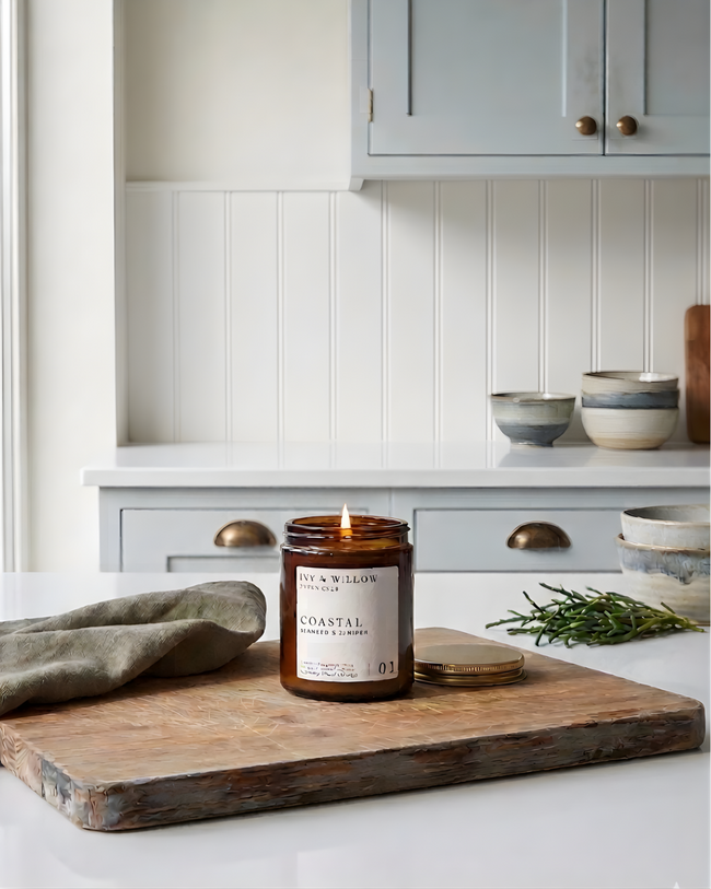 Candle on a wooden cutting board in a kitchen setting with bowls and cabinets.