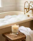 Bath tub with bubbles, candle, and towel in a bathroom setting