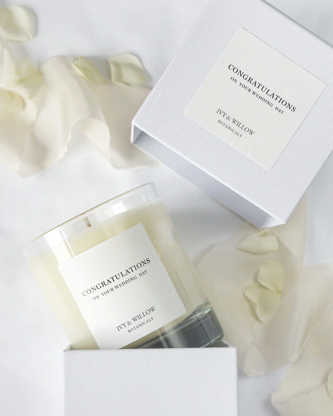 Candle with 'Congratulations' label and 'DIY & WILLOW' packaging on a white background with rose petals.