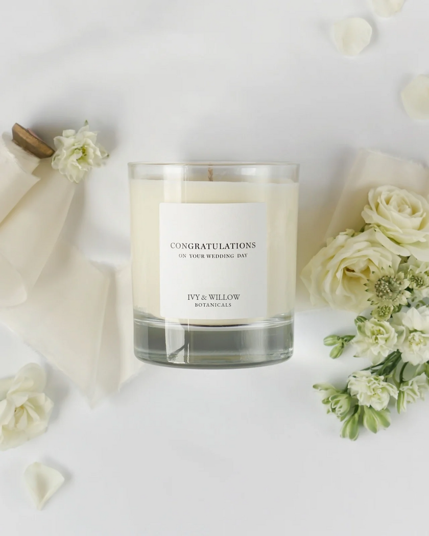 Candle with a 'Congratulations' message surrounded by white flowers on a light background