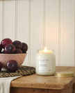 Candle labeled 'DAMSON' on a wooden surface with plums in the background