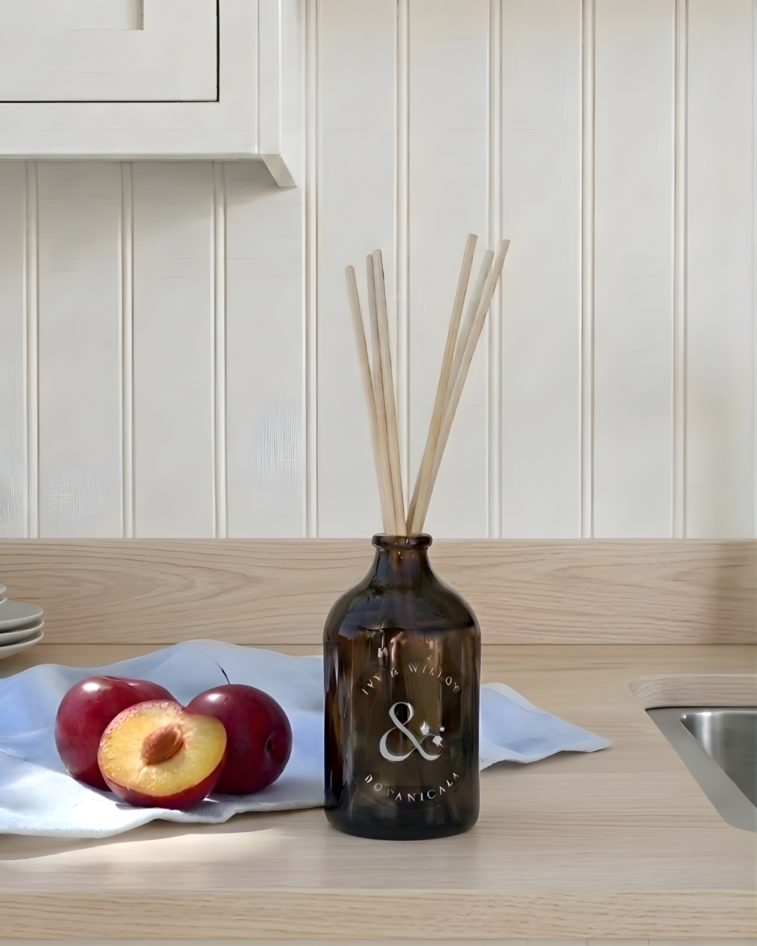 Brown diffuser bottle with sticks on a kitchen counter with apples and a white cloth.
