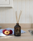 Brown diffuser bottle with sticks on a kitchen counter with apples and a white cloth.