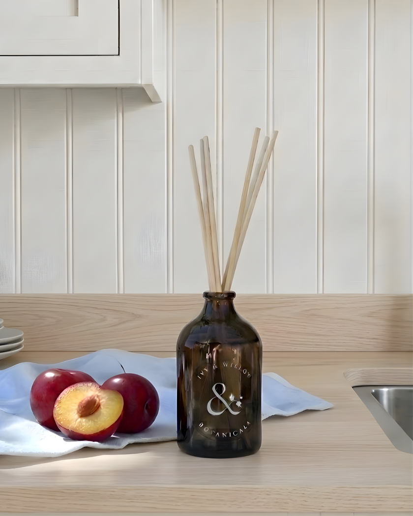 Brown diffuser bottle with sticks on a kitchen counter with apples and a white cloth.