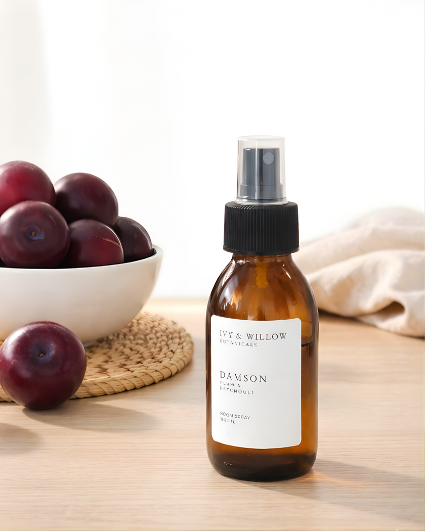 Brown spray bottle labeled 'Damson' on a wooden surface with plums and a towel in the background.