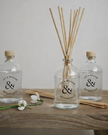 Two clear bottles with wooden sticks and a flower on a wooden surface, branded 'ivy & willow botanicales'.