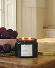 Black candle with a label on a wooden table next to plums