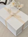White gift box with a beige ribbon and flowers on a light surface