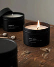 Candle in a black container labeled 'Havana' on a wooden surface with another candle in the background.