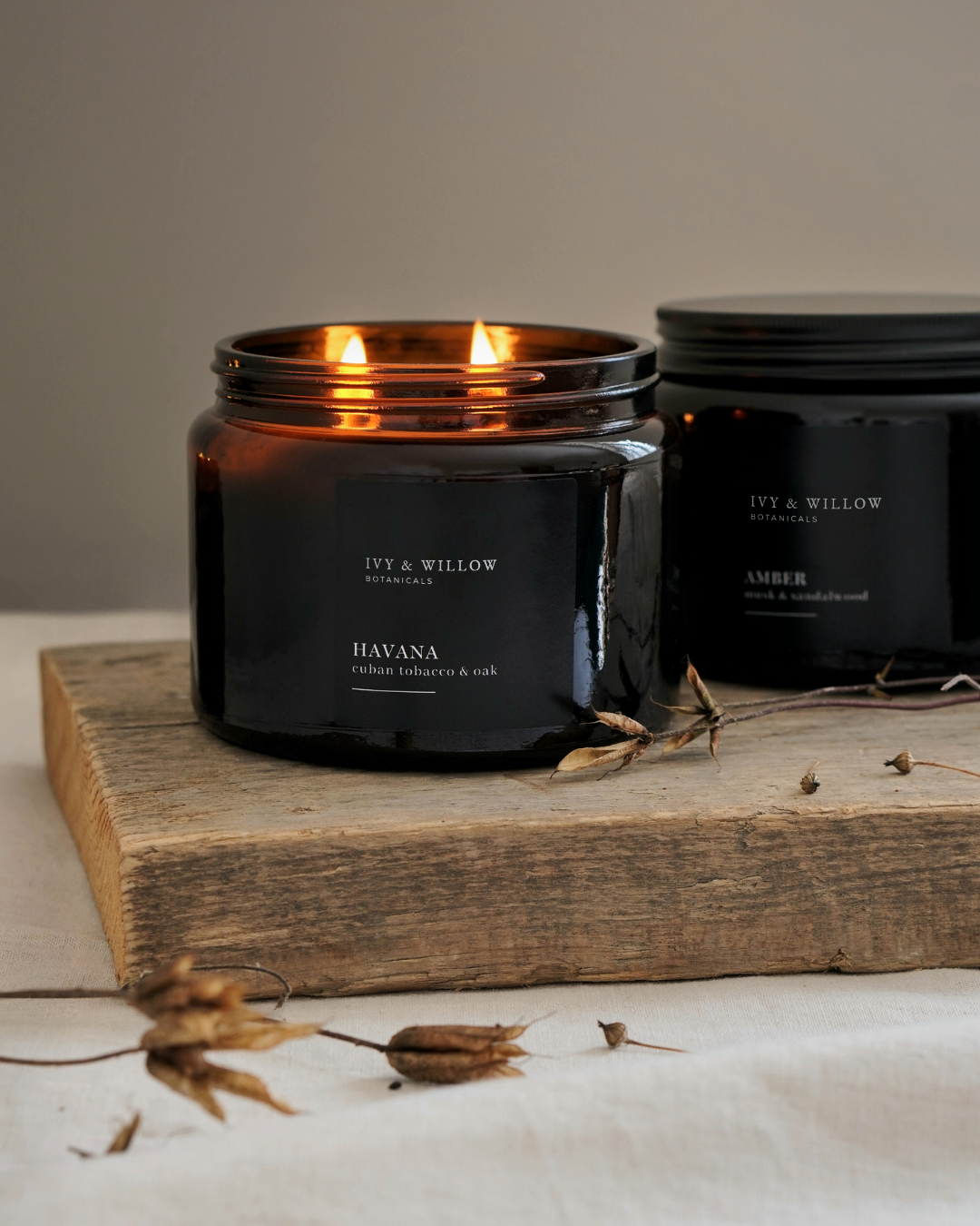 Black candle with 'Ivy & Willow' branding on a wooden surface with dried plants.
