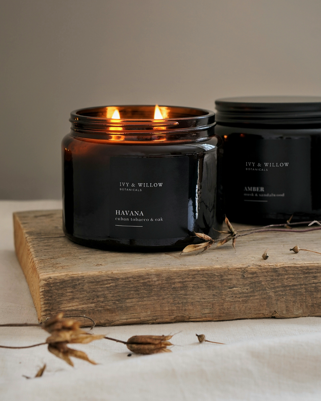 Black candle with 'Ivy & Willow' branding on a wooden surface with dried plants.