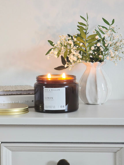 Candle with a label on a shelf next to a vase with flowers