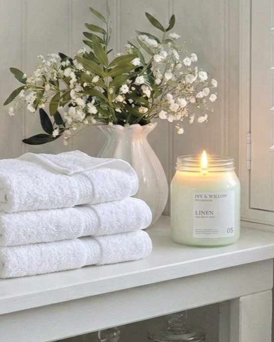 Stack of white towels with a candle and flowers on a white surface