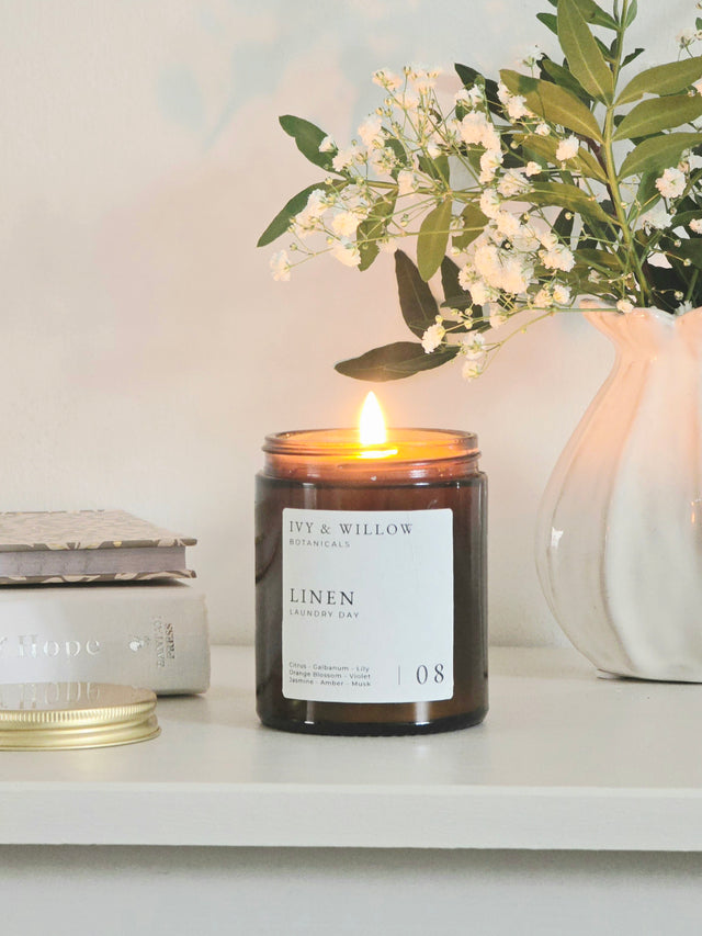 Candle with a label on a surface next to a vase with flowers