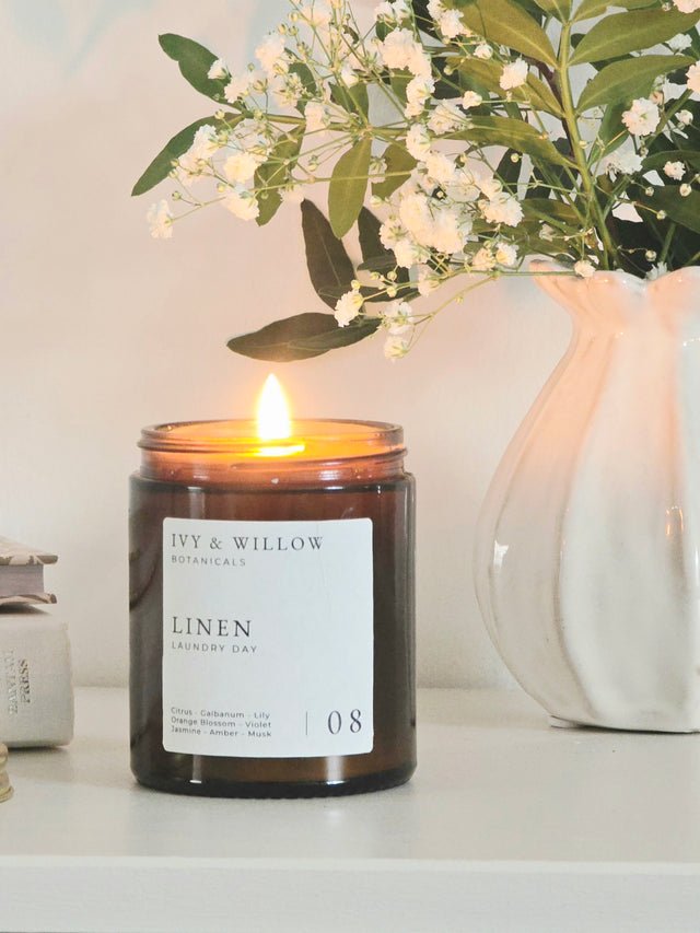 Candle with a label in front of a vase with flowers on a white surface