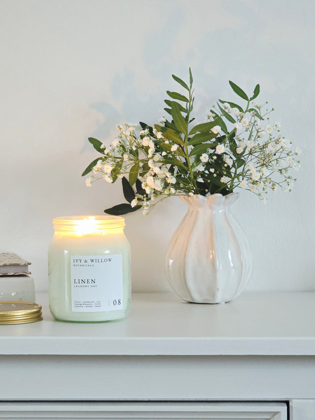 Candle with a label in front of a vase with flowers on a white surface