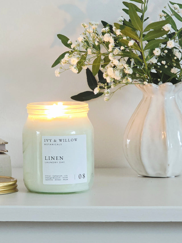 Candle labeled 'Ivy & Willow' on a shelf with a vase of flowers in the background