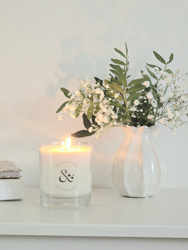 Candle with a logo and text in a white vase on a light surface with a light background