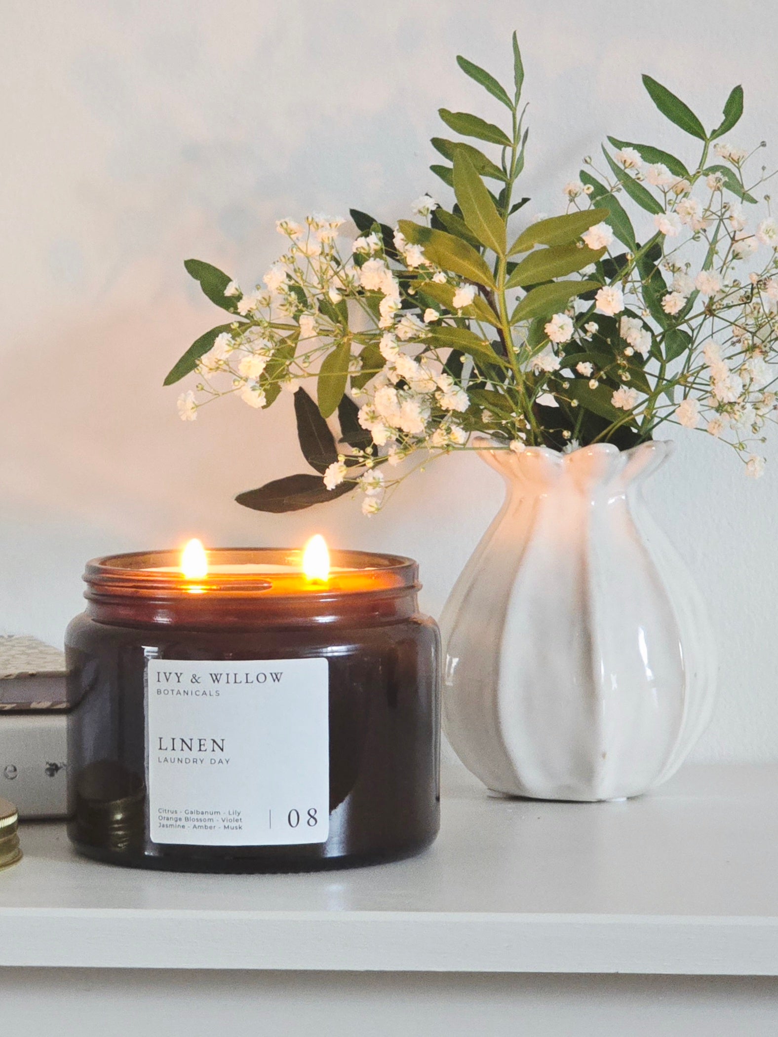 Candle with a label in front of a vase with flowers on a shelf