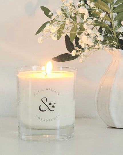 Candle with a brand logo next to a vase with flowers on a light background