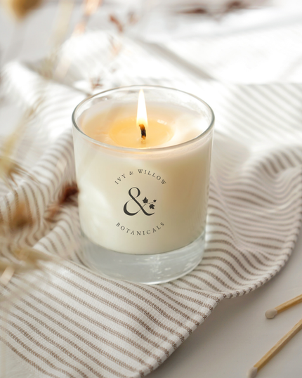 Candle in a glass jar with a brand logo on a textured surface