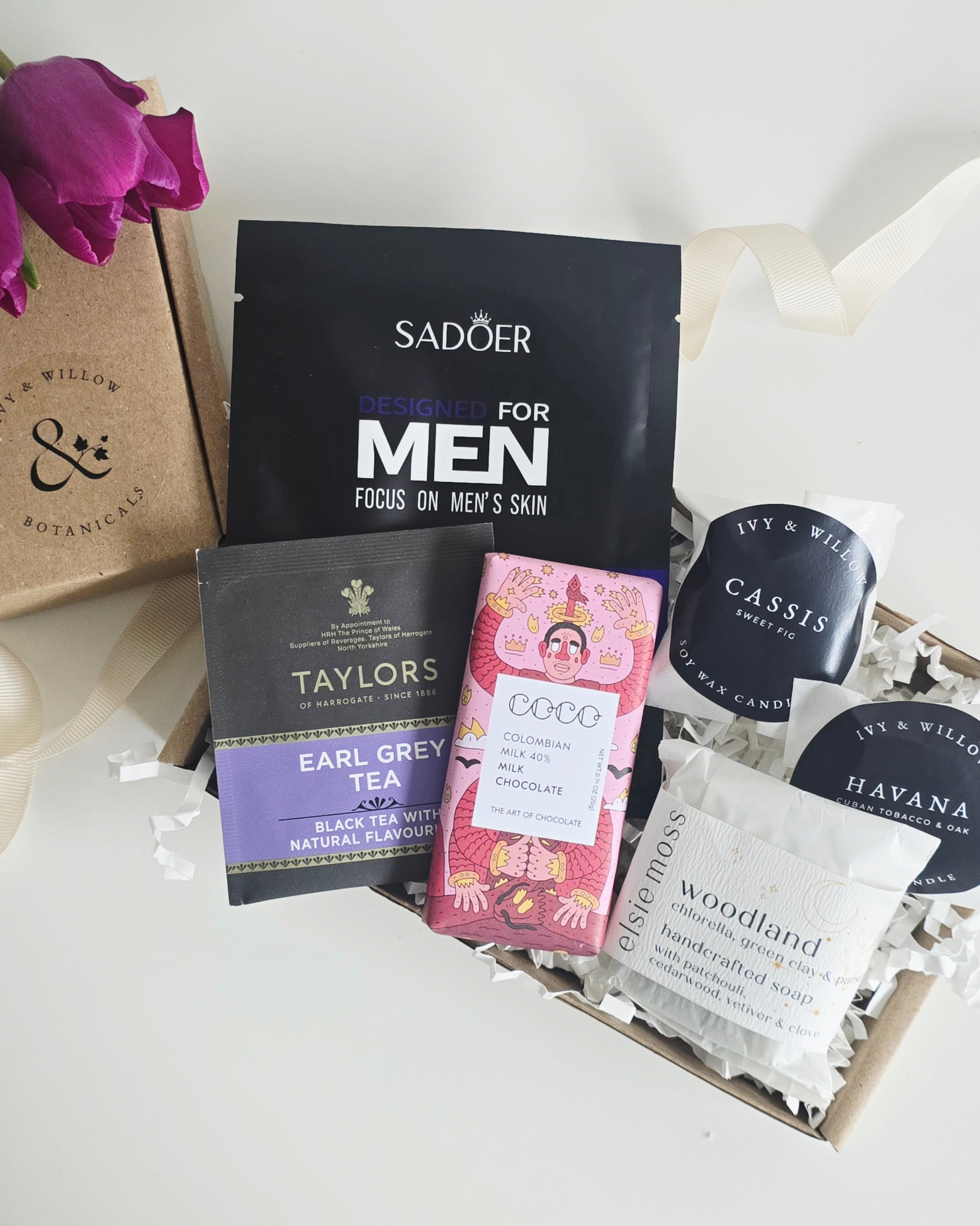 Collection of men's skincare products and tea packages on a white surface with a floral touch.