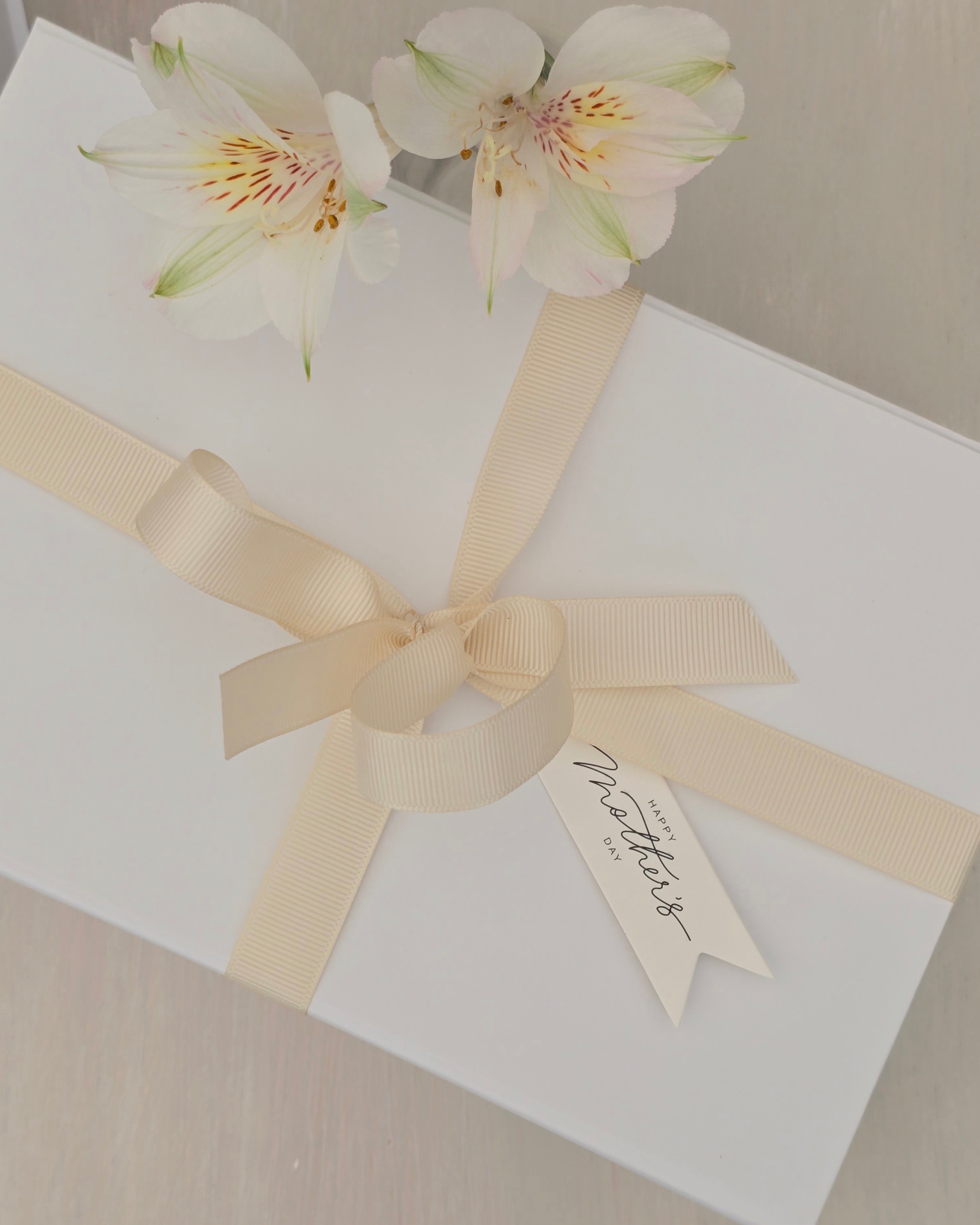 White gift box with a beige ribbon and floral decoration on a neutral background