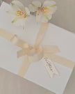 White gift box with a beige ribbon and floral decoration on a neutral background