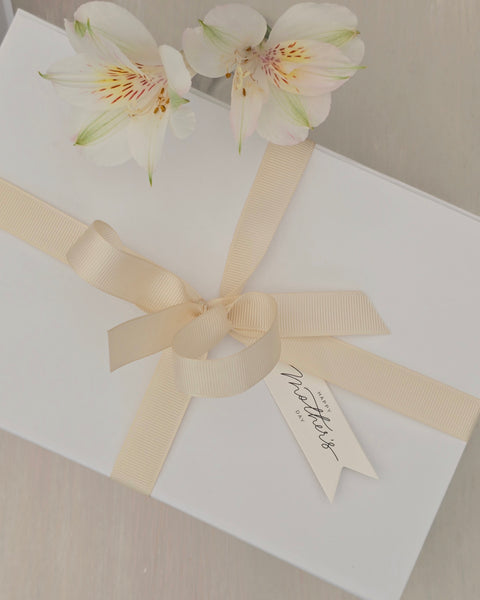 White gift box with a beige ribbon and floral decoration on a neutral background