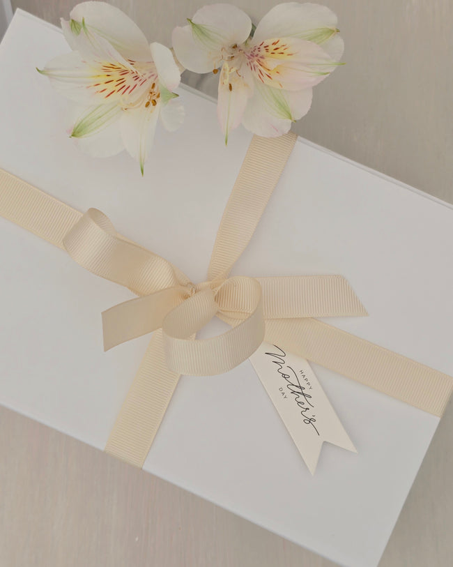 White gift box with a beige ribbon and floral decoration on a neutral background