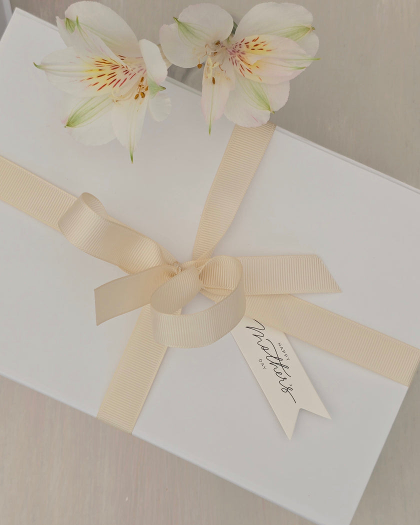 White gift box with a beige ribbon and floral decoration on a neutral background