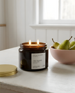 Candle in a jar labeled 'Orchard' by Ivy & Willow on a table with pears in the background.