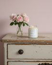 Candle and vase of flowers on a wooden dresser against a pink wall