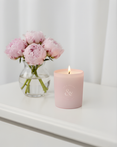 Pink candle and vase with pink peony flowers on a white surface